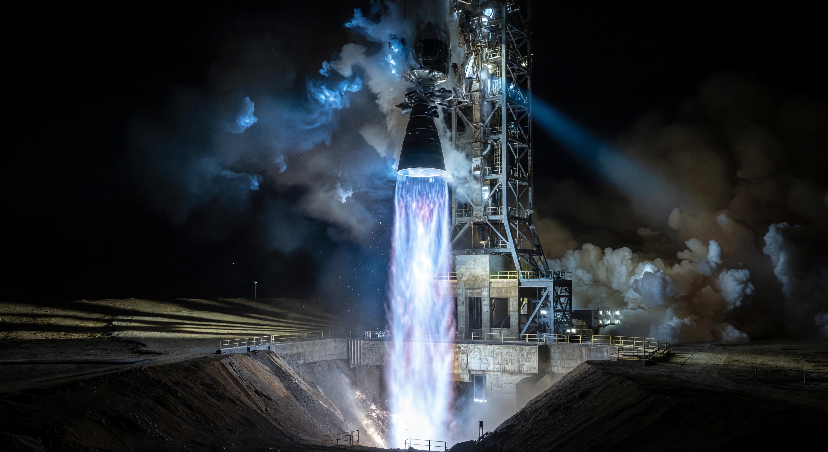 Rocket engine test fire at night showing bright blue-white exhaust plume